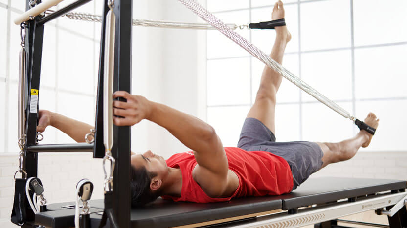 A young man practices Pilates on the Merrithew V2 Max Plus Reformer